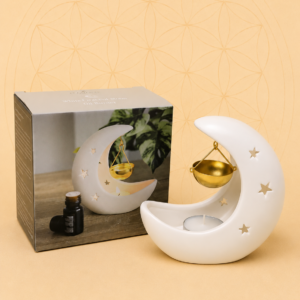 White crescent moon ceramic oil burner with a hanging golden bowl and gift box on a warm beige background.